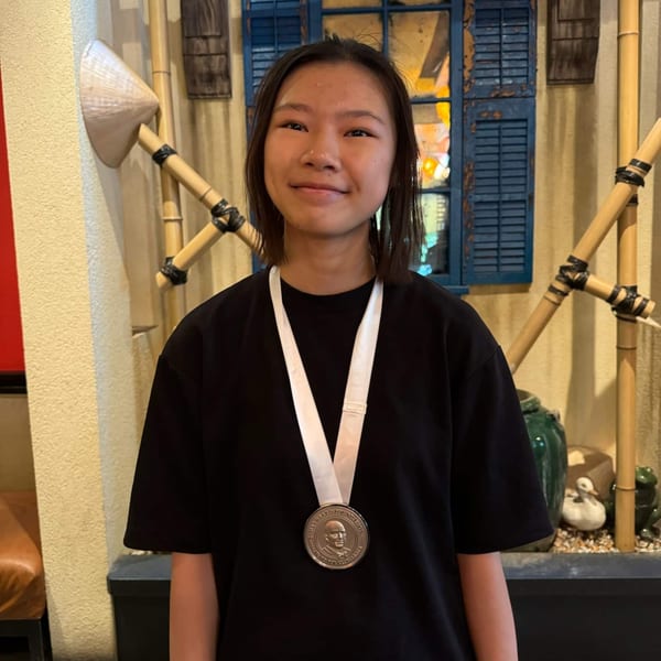 Young woman wearing a James Beard Foundation medal, smiling in front of Vietnamese decor.