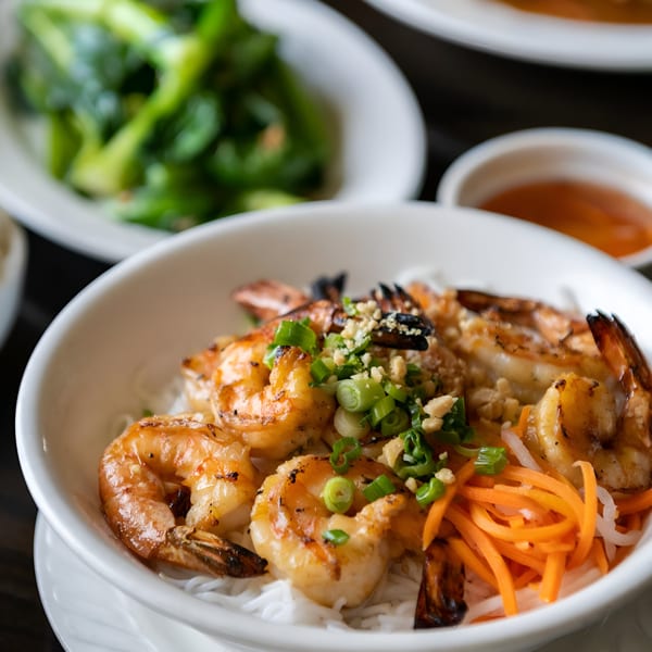 Grilled shrimp with vermicelli noodles, shredded carrots, and green onions in a white bowl.