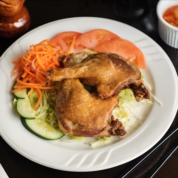 Crispy fried chicken legs with shredded carrots, sliced cucumbers, and tomatoes on a white plate.
