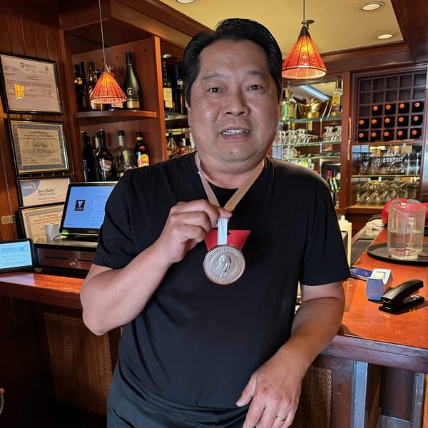 A man in a black shirt proudly displays a James Beard Foundation medal at Vietnam Philadelphia's bar.