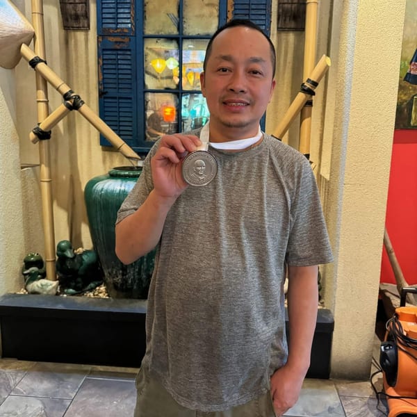 Man in a grey shirt holding a James Beard Foundation medal in a Vietnamese restaurant setting.