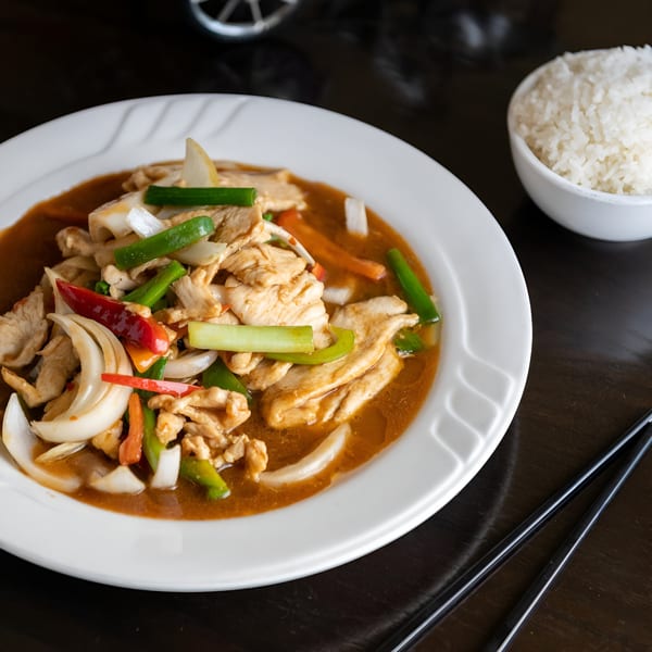 Chicken stir-fry with onions, peppers, and scallions in sauce, served with white rice and chopsticks.