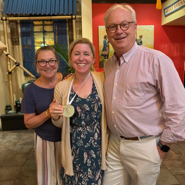 Three smiling people, one wearing a medal, standing in a Vietnamese restaurant with traditional decor.