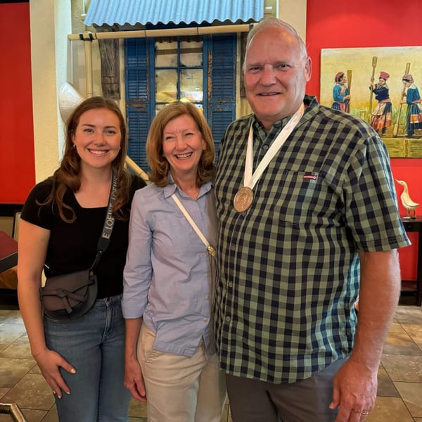 Three smiling people, two women and one man, stand together in a Vietnamese restaurant.