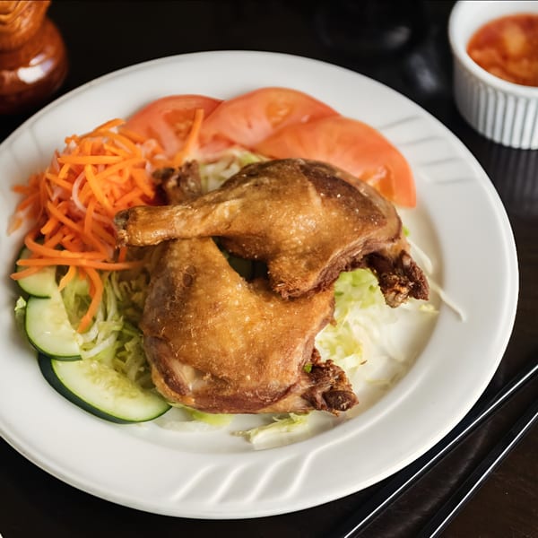 Crispy fried chicken legs with shredded lettuce, carrots, cucumbers, and tomato slices on a white plate.