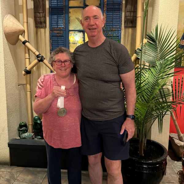 A smiling woman with a medal and a man stand in a Vietnamese restaurant with bamboo decor.