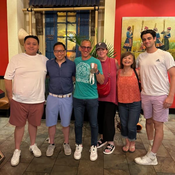 Six smiling people, including one holding a medal, stand in front of a Vietnamese-themed mural.